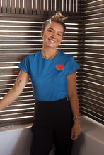 Charger l'image dans la galerie, mannequin-ravissante-femme-qui-sourit-et-qui-porte-un-tshirt-pasteque-bleu-ohmyfruits-dans-une-piece-en-bois