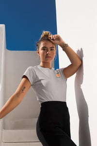 modele-sublime-femme-qui-porte-un-tshirt-gris-peche-ohmyfruits-et-quipose-dans-un-escalier-blanc-avec-le-ciel-bleu