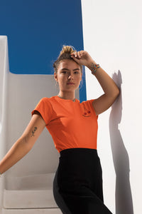 modele-sublime-femme-qui-porte-un-tshirt-orange-cerise-ohmyfruits-et-quipose-dans-un-escalier-blanc-avec-le-ciel-bleu